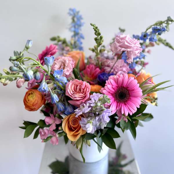 Colorful mixed bouquet in a white vase with pink, orange, blue, and purple blooms