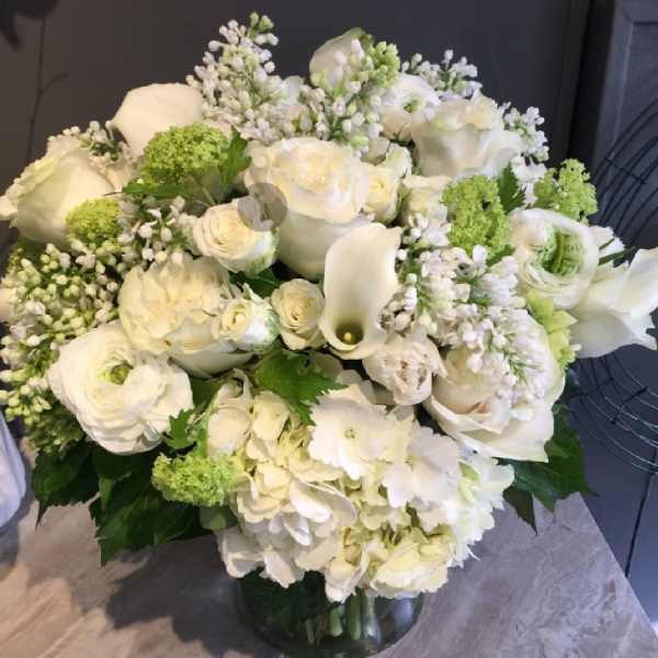 White floral arrangement with roses, calla lilies, and hydrangeas in a glass vase