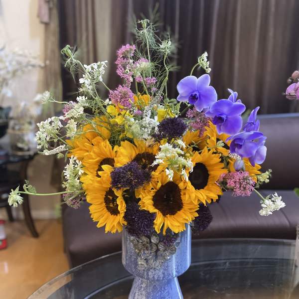 Sunflowers and purple orchids arranged in a blue vase