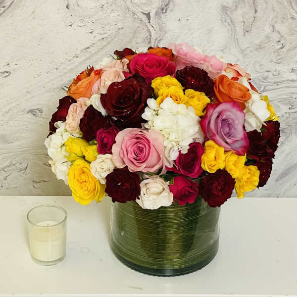 Mixed roses in a green glass vase beside a small candle