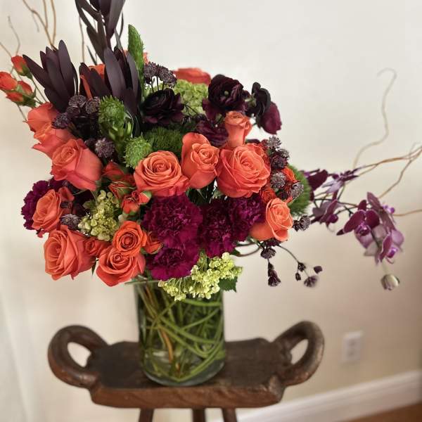Coral roses and dark purple flowers arranged in a glass vase