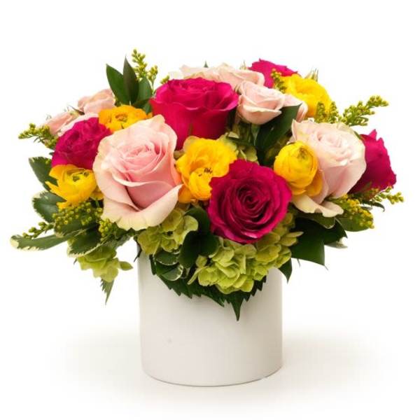 Low arrangement of pink and hot pink roses with yellow blooms and green hydrangea in a white cylinder vase