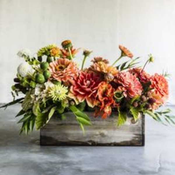 Low floral arrangement in a wooden box with orange and pink blooms