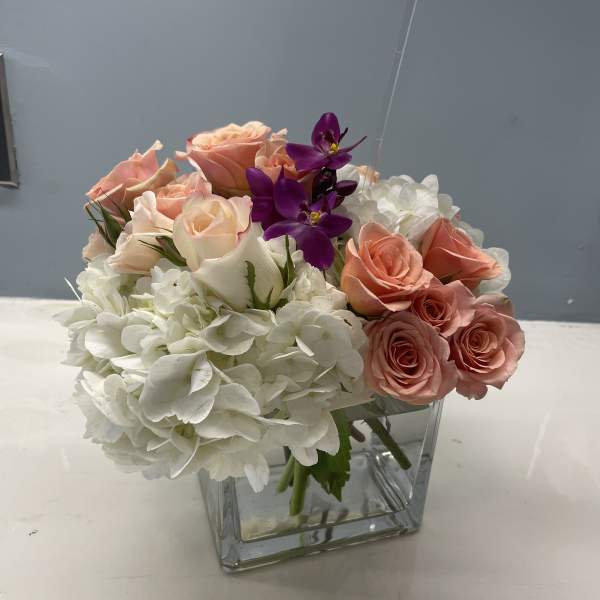Pink roses and white hydrangeas in a clear square vase with purple orchids