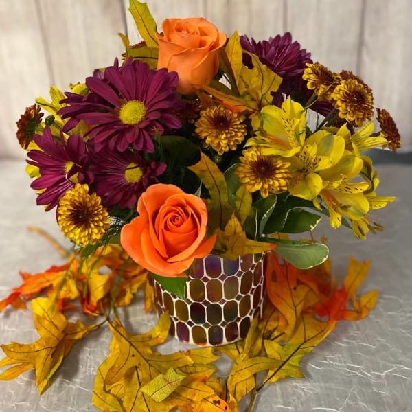 Orange roses and purple daisies in a patterned vase with autumn leaves