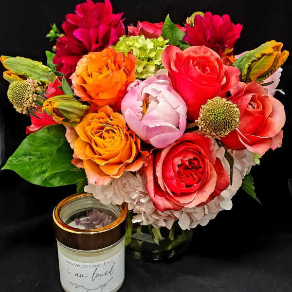 Bright mixed bouquet with roses, peonies, and hydrangeas beside a candle