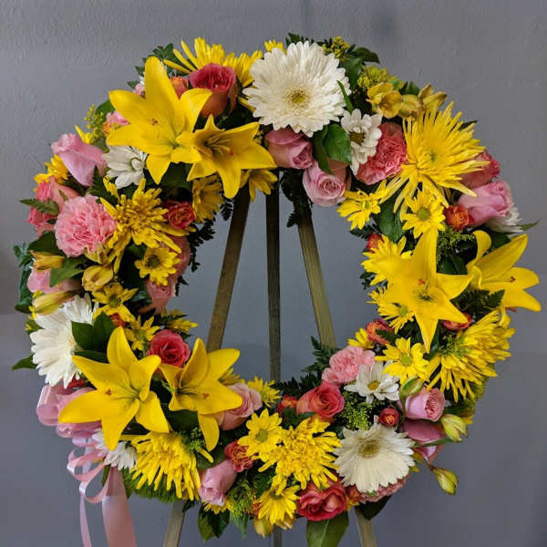 Circular floral wreath with yellow lilies, pink roses, and white daisies on an easel