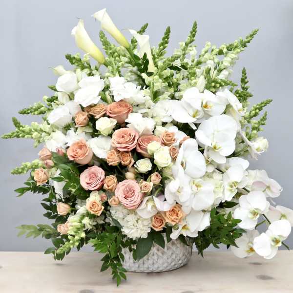Large arrangement of white orchids, calla lilies, and peach and cream roses in a white vase