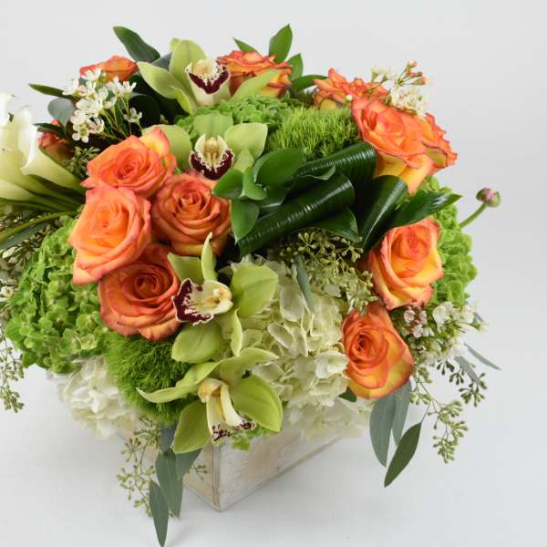 Orange roses and white lilies arranged in a square vase