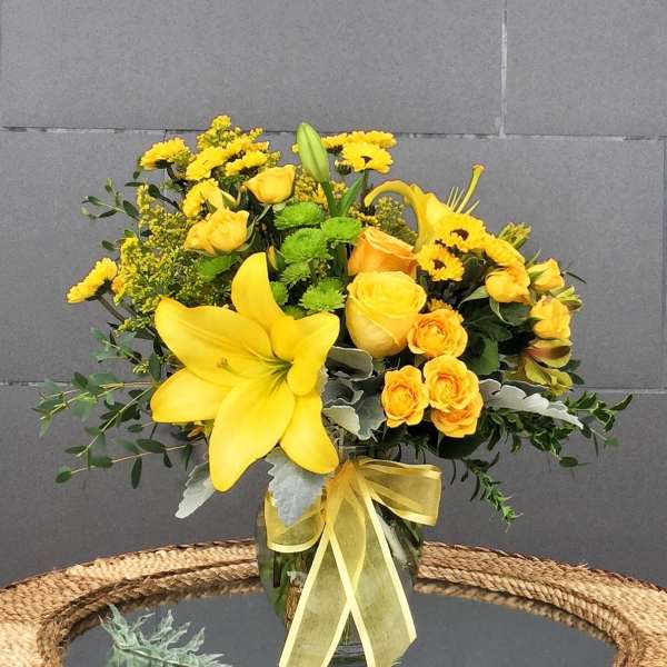 Yellow floral arrangement in a glass vase with a ribbon
