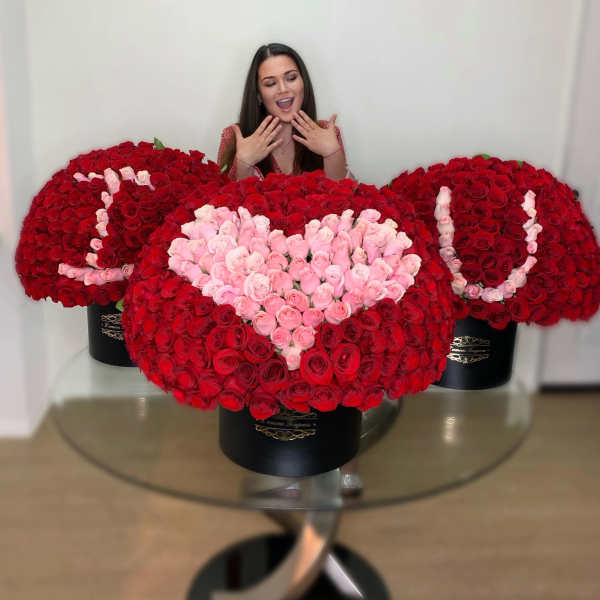 Three large red and pink rose hatbox arrangements spelling I heart U on a glass table