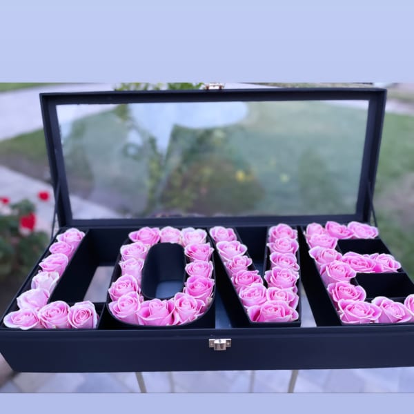 Pink roses arranged to spell LOVE in a black box