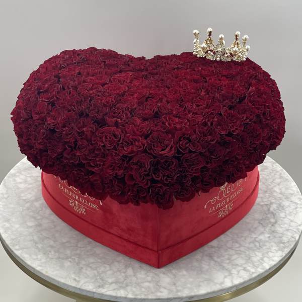 Heart-shaped box of deep red roses with a small crown topper