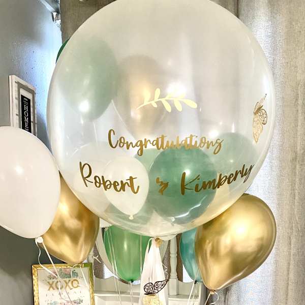 Cluster of gold, white, and green balloons with a large clear balloon reading congratulations