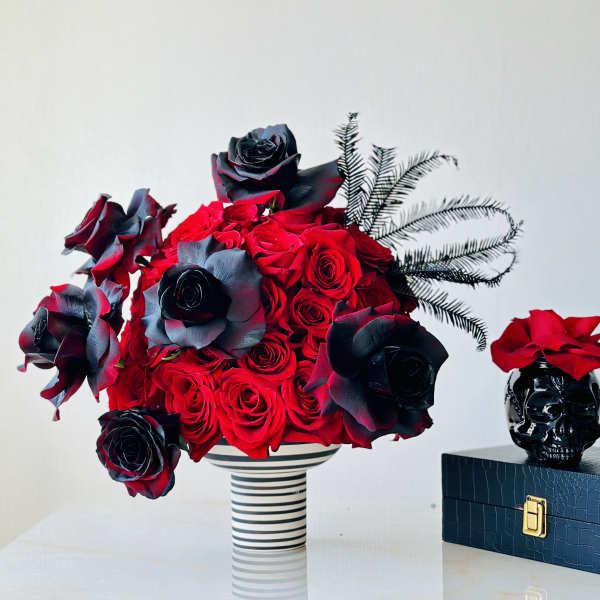 Red and black roses arranged in a striped vase beside a skull decoration