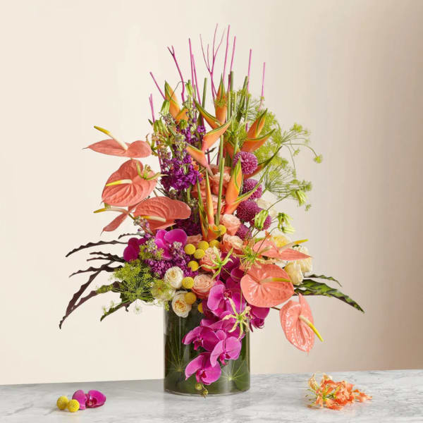 Tall tropical arrangement in a glass vase with pink anthuriums and orchids