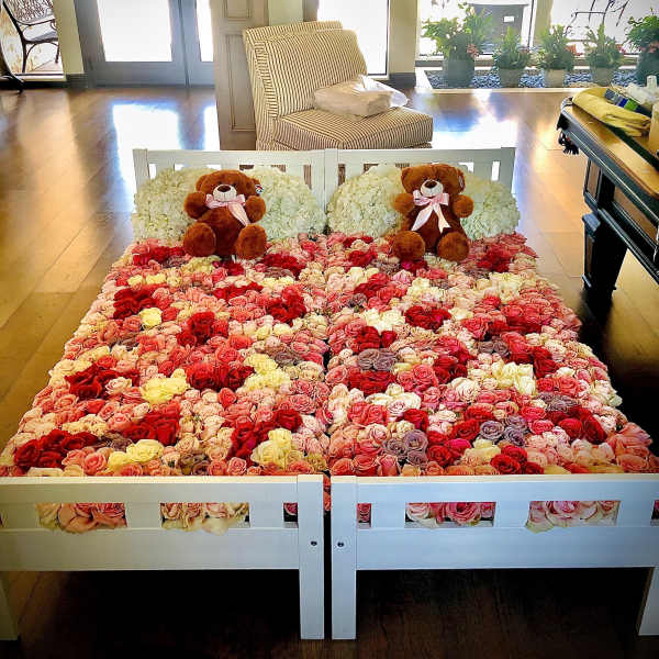 Bed covered in multicolored roses with two teddy bears at the headboard