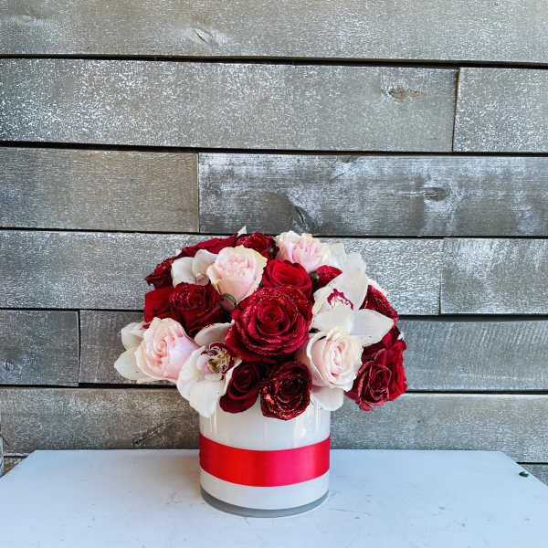 Red and blush roses arranged in a white hatbox with a pink ribbon