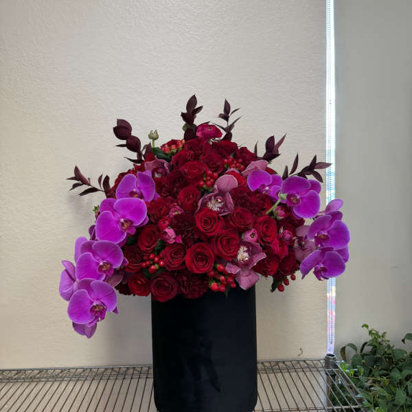 Red rose and purple orchid arrangement in a black cylinder vase