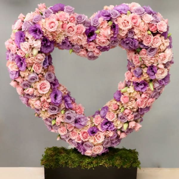 Large heart-shaped arrangement of pink and purple flowers on a moss-covered black rectangular base