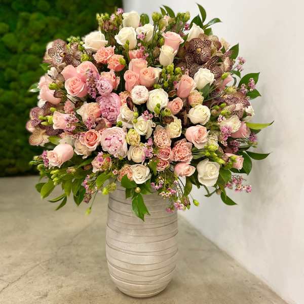 Large arrangement of pink and white roses, peonies, and mixed blooms in a tall cream ceramic vase