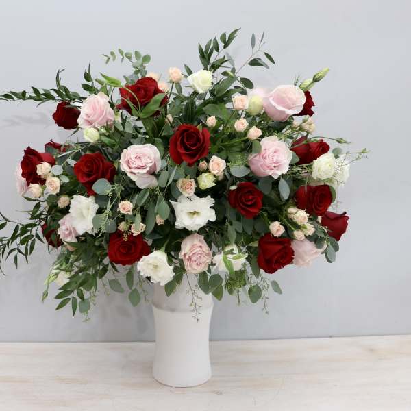 Tall vase of red, pink, and white roses with filler blooms in a lush, wide arrangement