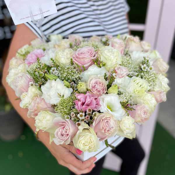 Handheld bouquet of pale pink and white roses with small filler flowers