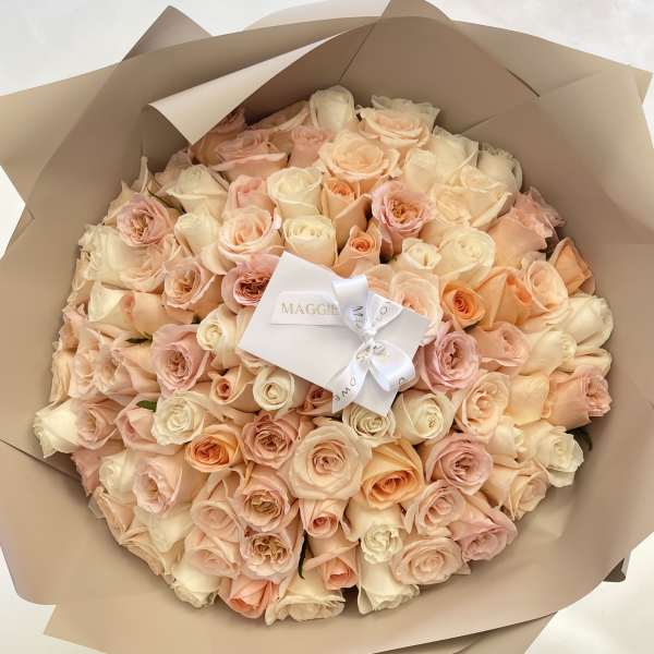 Bouquet of blush and cream roses wrapped in tan paper with a white ribbon