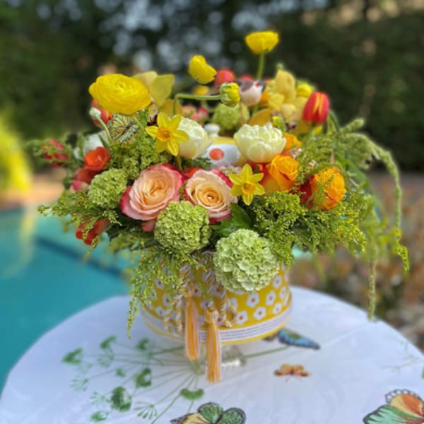 Bright yellow and peach floral arrangement in a patterned container
