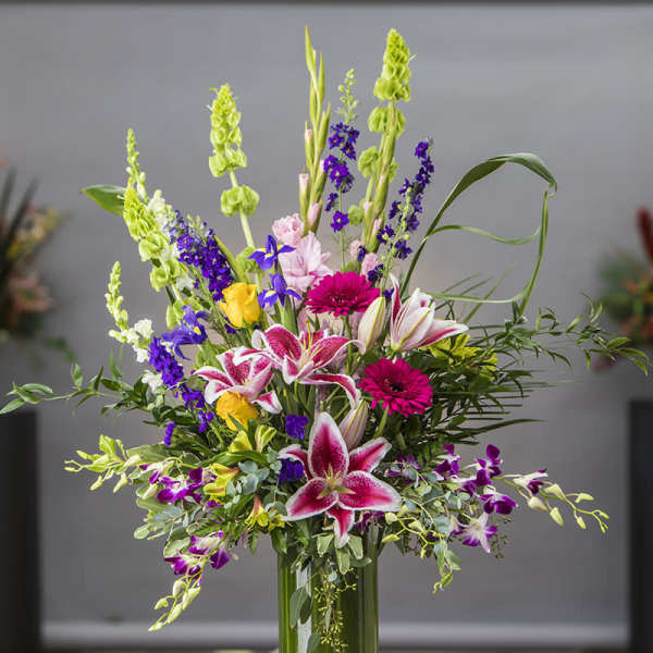 Tall mixed bouquet with lilies, orchids, and bright purple flowers in a glass vase
