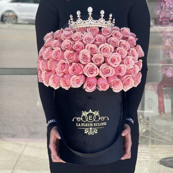 Large bouquet of pink roses in a black hatbox with a jeweled crown topper