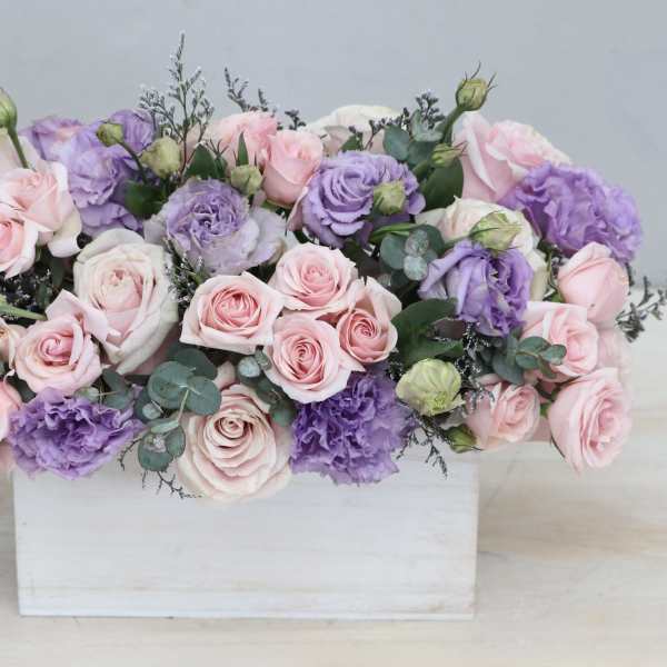 Low arrangement of pink roses and lavender lisianthus in a white wooden box