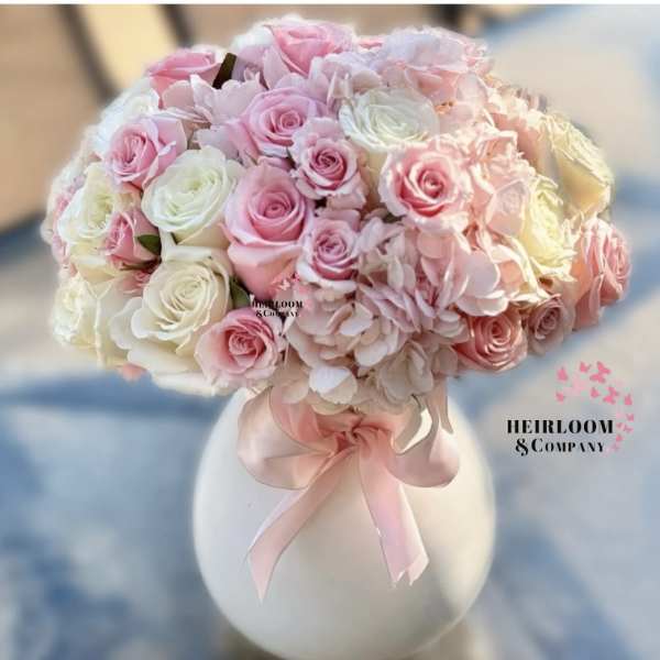 Pink and white rose bouquet in a white vase with a pink ribbon