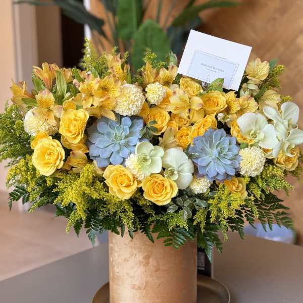 Yellow roses and orchids arranged in a gold hatbox