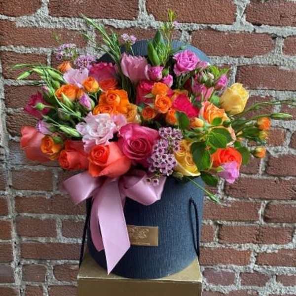 Mixed bouquet of roses and small filler flowers in a dark hatbox with a pink ribbon