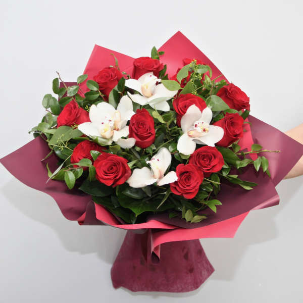 Hand-tied bouquet of red roses and white orchids wrapped in burgundy and pink paper