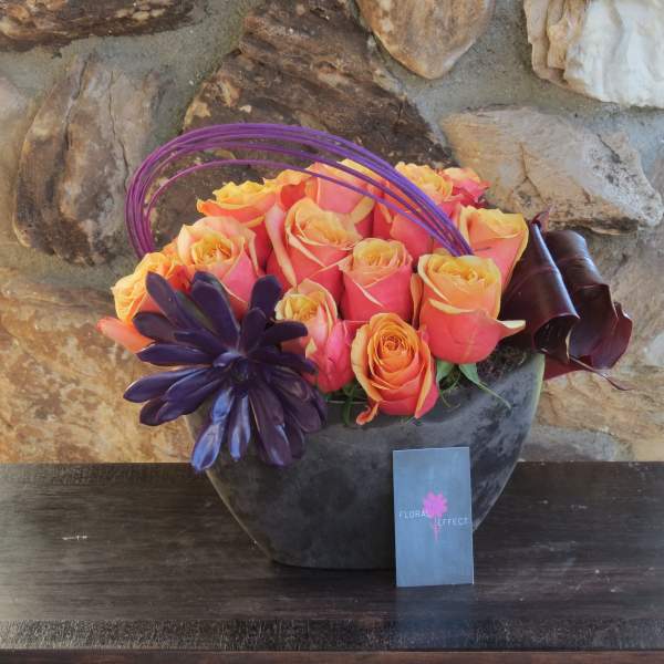 Orange and pink roses in a dark vase with purple decorative accents