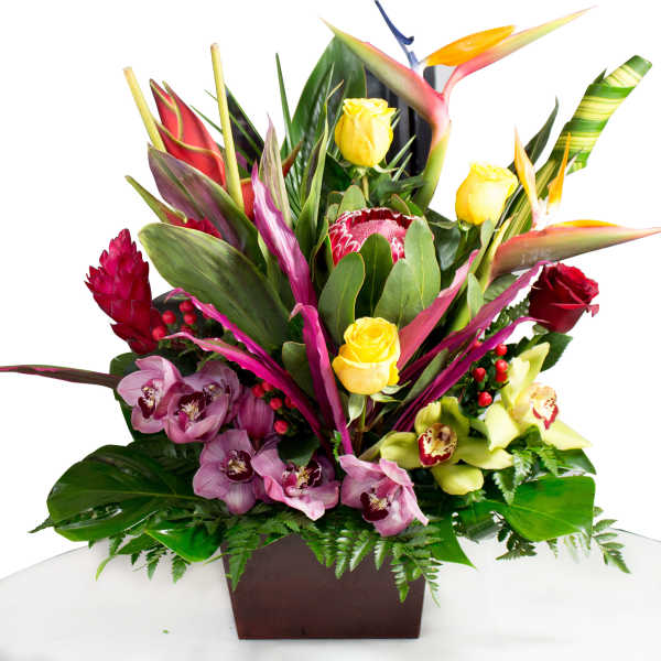 Tropical floral arrangement with yellow roses and orchids in a dark square vase