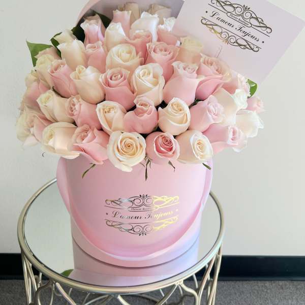 Round box of pale pink and cream roses with a card on a mirrored side table