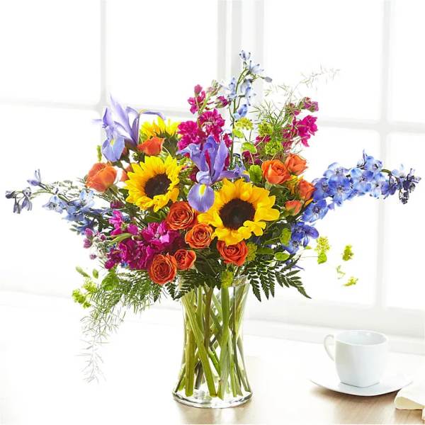 Colorful bouquet with sunflowers, roses, and blue irises in a glass vase