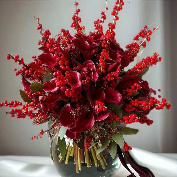 Deep red floral arrangement in a glass vase with berry branches and ribbon
