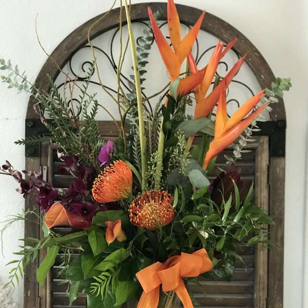 Tropical bouquet with orange bird-of-paradise and orange pincushion blooms in a glass vase