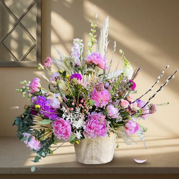 Large pink and purple floral arrangement in a light wood vase