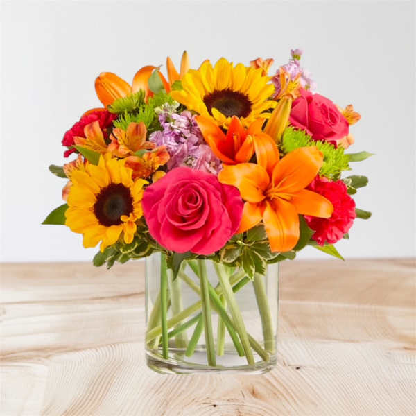 Bright mixed bouquet with sunflowers, roses, and lilies in a glass vase