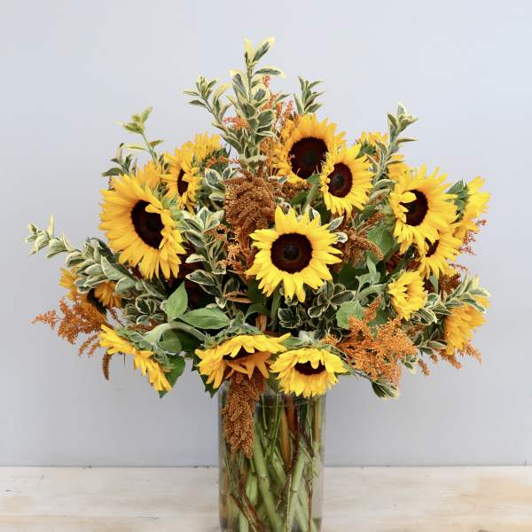Tall glass vase of yellow sunflowers with orange filler blooms and variegated foliage