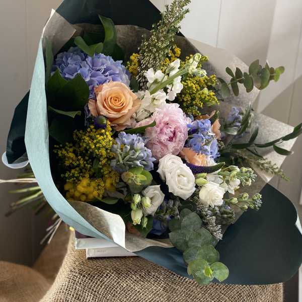 Mixed bouquet with hydrangea, roses, and pastel blooms wrapped in dark paper