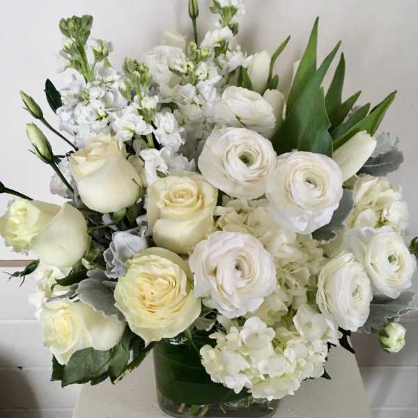 White roses and ranunculus in a glass vase with white filler flowers