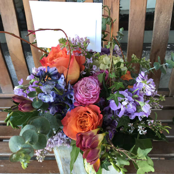 Mixed bouquet with orange and purple roses in a white container
