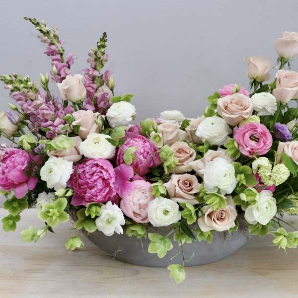 Low oval centerpiece of pink peonies, blush roses and white ranunculus in a gray container