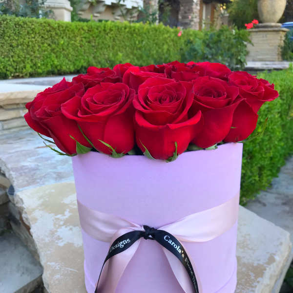 Red roses arranged in a lavender hat box with a ribbon bow